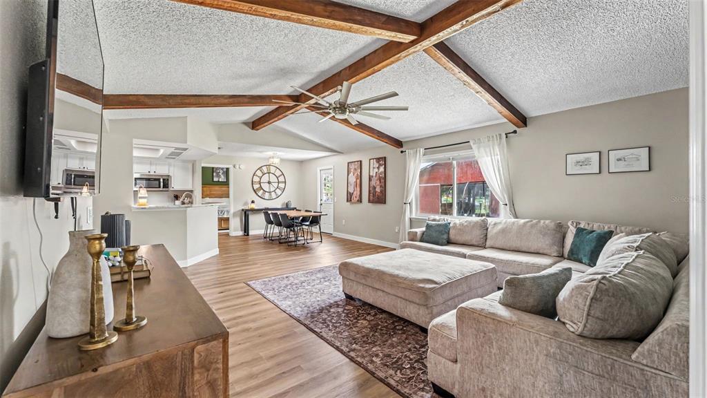 A living room with wood-beamed vaulted ceilings, light wood flooring, and an adjacent dining area — 5303 KNIGHTS STATION ROAD, LAKELAND, FL