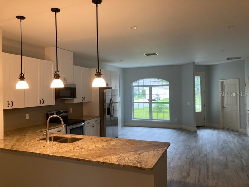 A kitchen with granite countertops and pendant lights overlooks an open living area with tile floors — 20 ETON LANE UNIT A, PALM COAST, FL