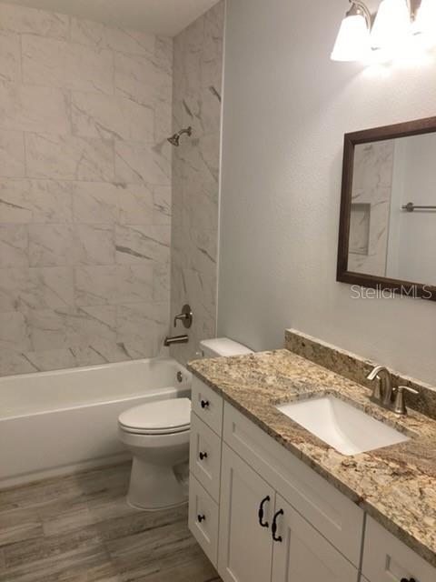 A bathroom features a marble-tiled shower, a granite-topped vanity, and a white toilet — 20 ETON LANE UNIT A, PALM COAST, FL
