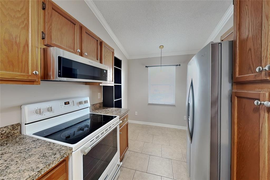 A kitchen features wood cabinets, stainless steel appliances, granite countertops, and light tile flooring — 111 HIDDEN ARBOR COURT, SANFORD, FL