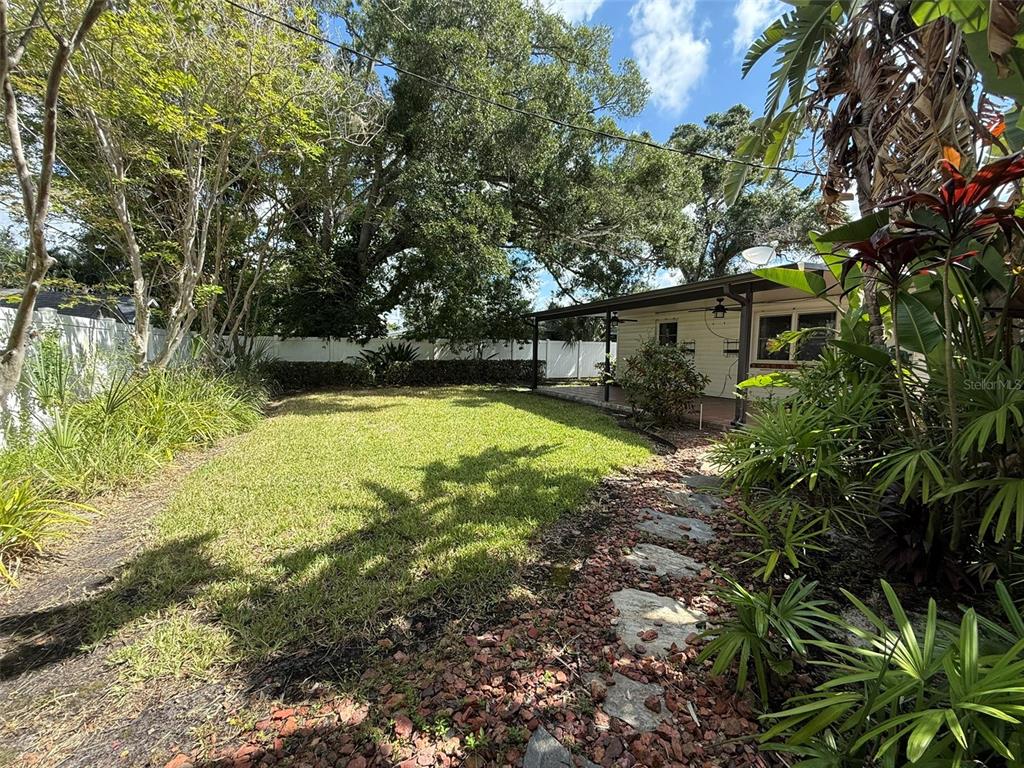 A grassy backyard features a stone path, tropical landscaping, and a covered patio area — 215 S WEST SHORE BOULEVARD, TAMPA, FL