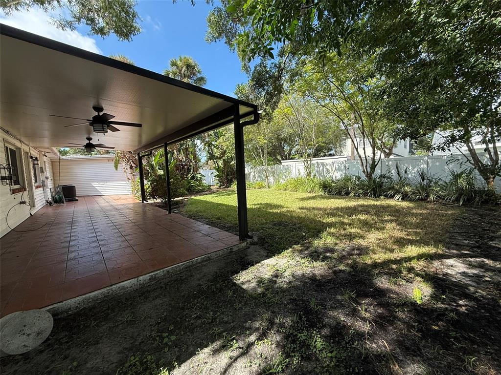 A covered patio with tiled flooring and ceiling fans overlooks a grassy backyard with trees — 215 S WEST SHORE BOULEVARD, TAMPA, FL