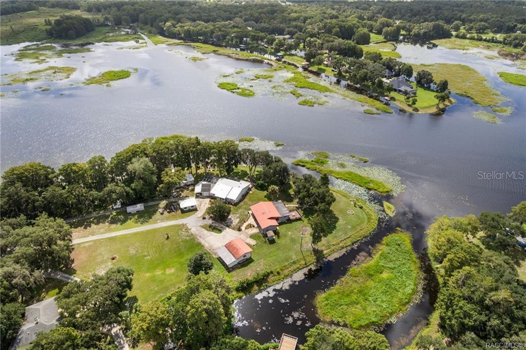 An aerial view shows a waterfront property with several buildings, a driveway, and surrounding trees — 8004 E HALCYON ISLE COURT, INVERNESS, FL