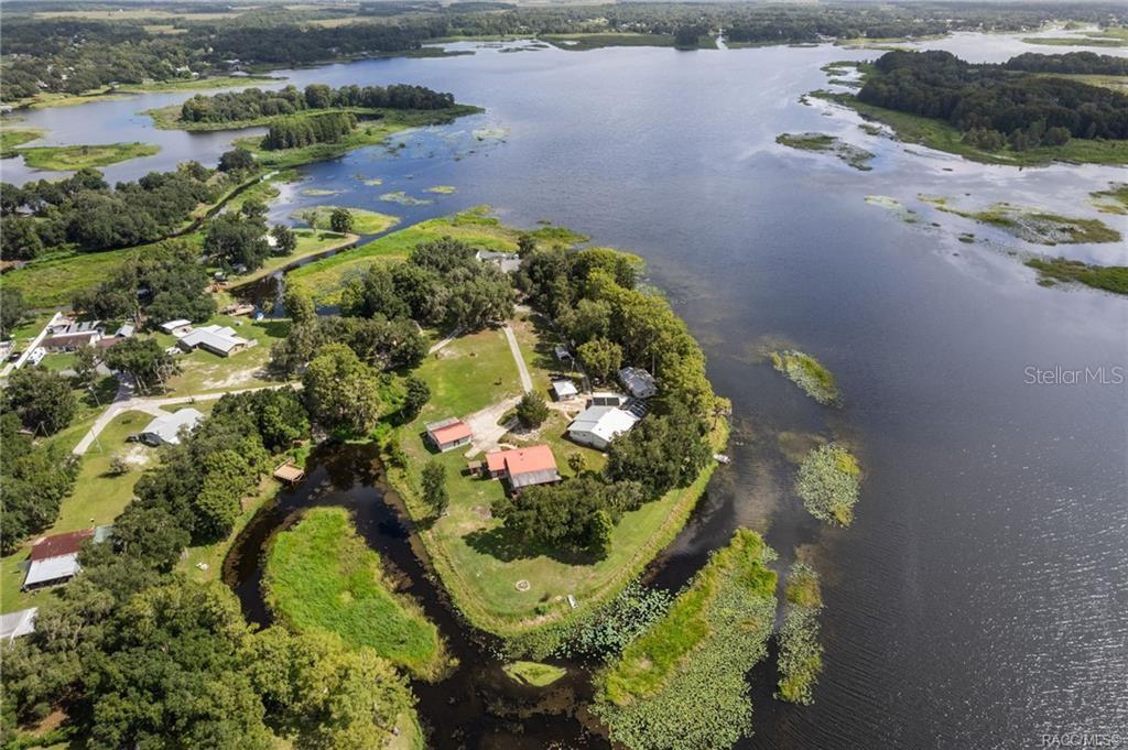 An aerial view shows a house and outbuildings on a peninsula surrounded by a lake — 8004 E HALCYON ISLE COURT, INVERNESS, FL