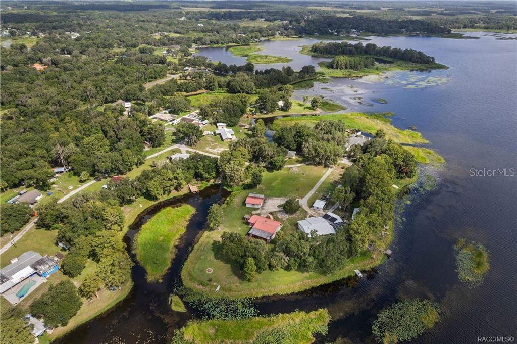 An aerial view shows a waterfront property with several buildings surrounded by trees and water — 8004 E HALCYON ISLE COURT, INVERNESS, FL