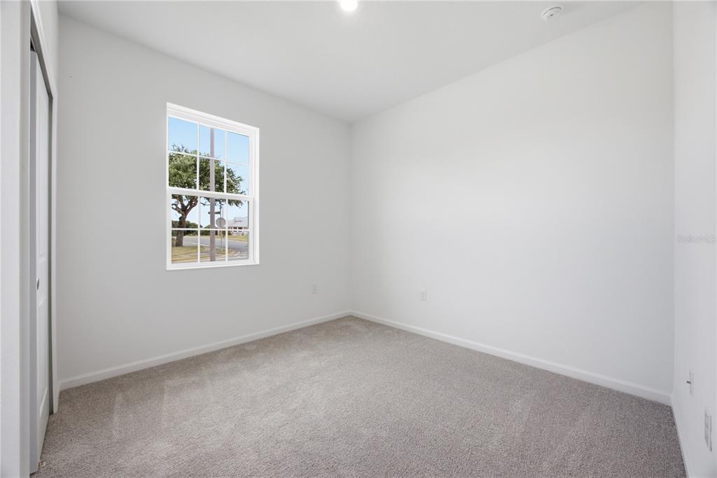 An empty bedroom features white walls, gray carpet, and a single window — 6205 SANDERS GROVE CIRCLE, OKAHUMPKA, FL