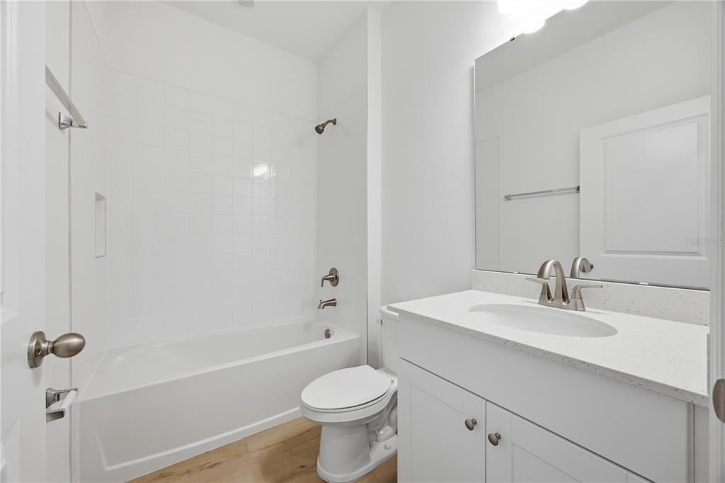 A bathroom features a white vanity, a toilet, and a bathtub with a tiled surround — 6205 SANDERS GROVE CIRCLE, OKAHUMPKA, FL
