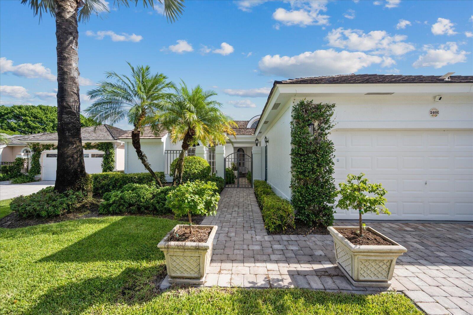 A paved walkway leads to the front gate of a white house with palm trees — 2466 Muir Circle, Wellington FL 33414, WELLINGTON, FL