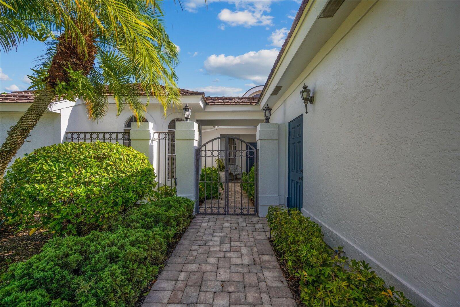 A paved walkway leads through a metal gate to the entrance of a white house — 2466 Muir Circle, Wellington FL 33414, WELLINGTON, FL