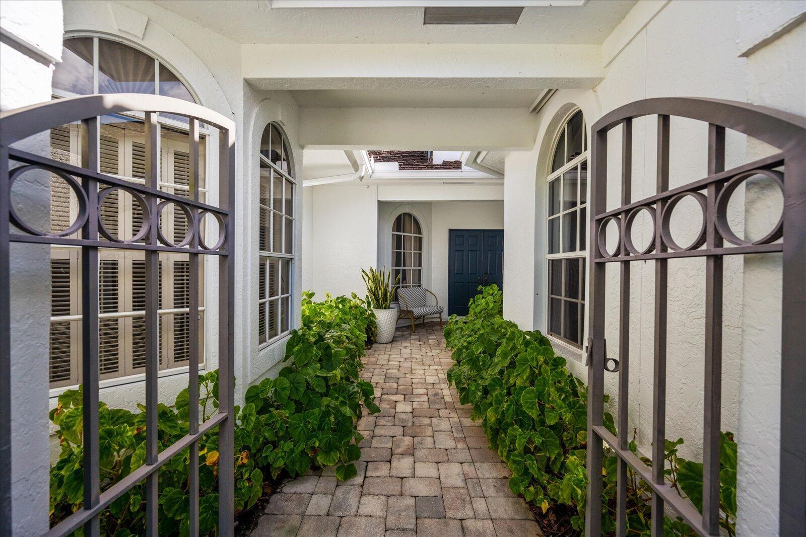 A paved walkway leads through a gated entrance toward a blue front door — 2466 Muir Circle, Wellington FL 33414, WELLINGTON, FL