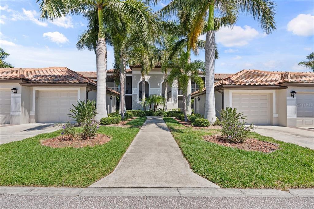 A sidewalk leads to the entrance of a two-story residential building with two attached garages — 6705 GRAND ESTUARY TRAIL UNIT 104, BRADENTON, FL