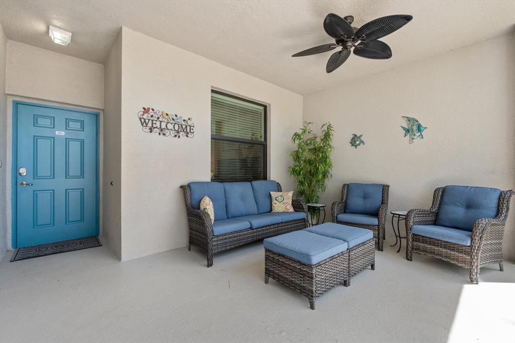 A covered patio features wicker furniture with blue cushions, a ceiling fan, and a blue door — 6705 GRAND ESTUARY TRAIL UNIT 104, BRADENTON, FL