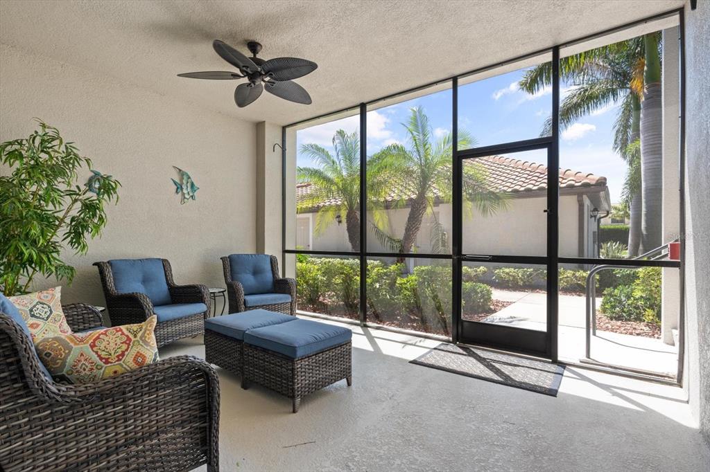 A screened-in patio features wicker furniture, a ceiling fan, and views of palm trees — 6705 GRAND ESTUARY TRAIL UNIT 104, BRADENTON, FL