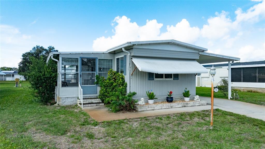 A single-story manufactured home with a screened-in porch, metal awning, and a carport — 706 LEWARD WAY, PORT ORANGE, FL