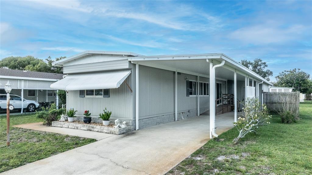A light gray mobile home features a metal awning, a concrete driveway, and a carport — 706 LEWARD WAY, PORT ORANGE, FL