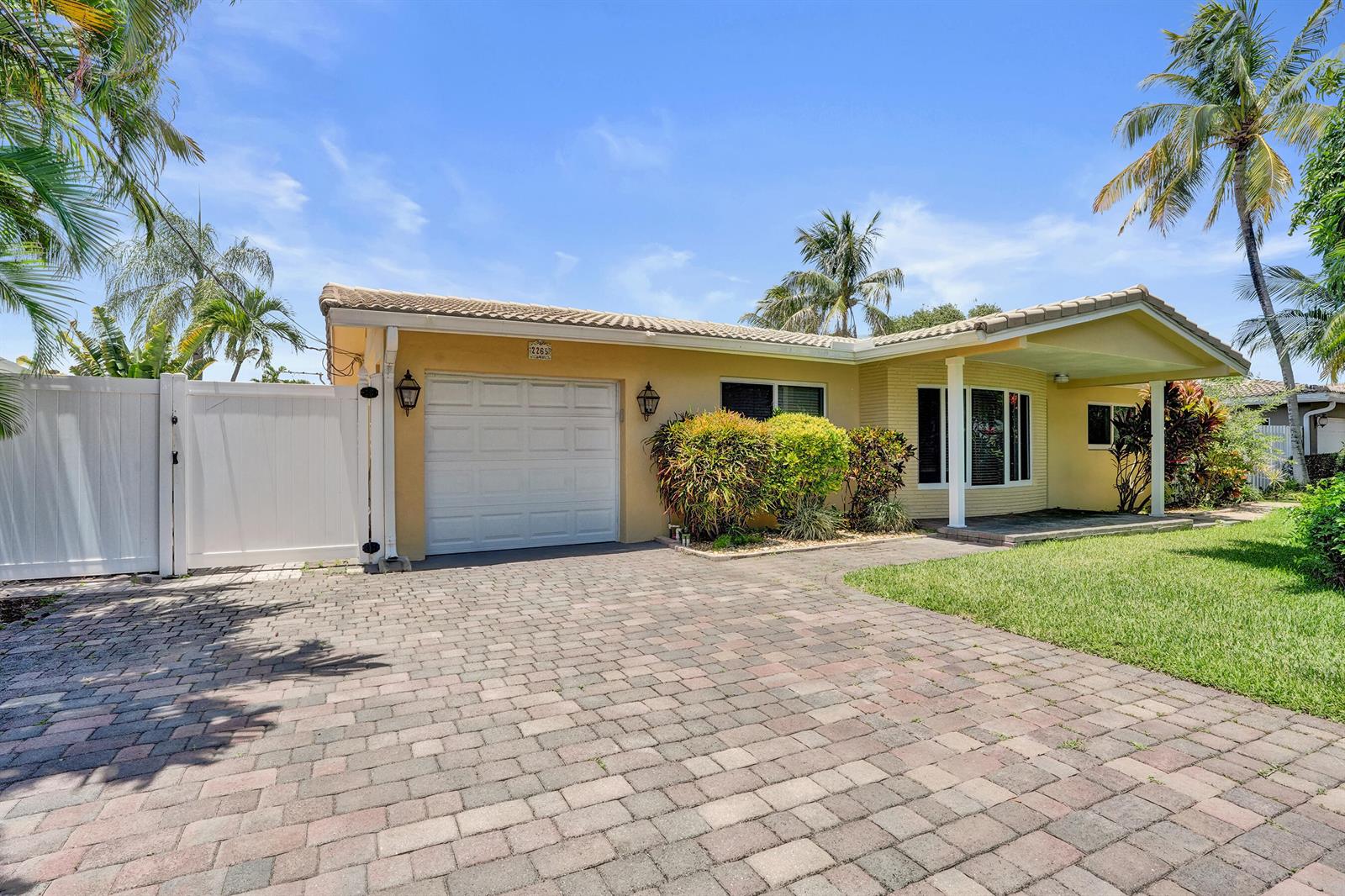 A yellow single-story house with a paved driveway, white fence, and palm trees — 2265 SE 12th Street, Pompano Beach FL 33062, POMPANO BEACH, FL