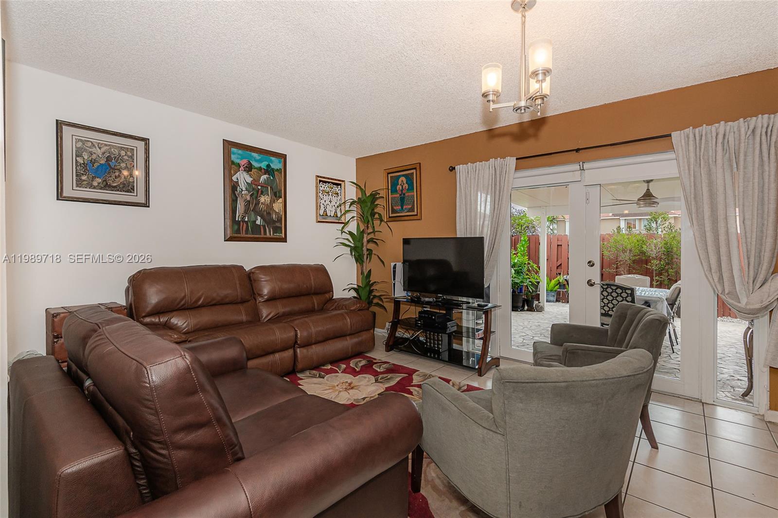 A living room features brown leather sofas, gray armchairs, a television, and glass patio doors — 17757 SW 141st Ct, Miami FL 33177, MIAMI, FL