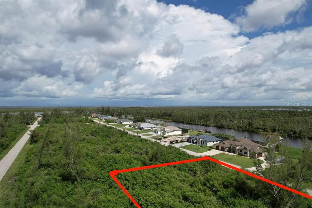 An aerial view shows a vacant, brush-covered lot outlined in red near waterfront homes — 16733 LIGGETT CIRCLE, PORT CHARLOTTE, FL