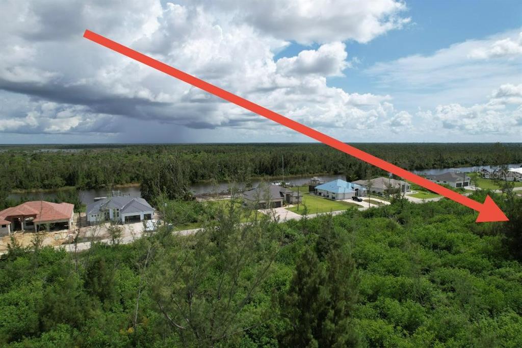 An aerial view shows a vacant, wooded lot next to several houses near a canal — 16733 LIGGETT CIRCLE, PORT CHARLOTTE, FL