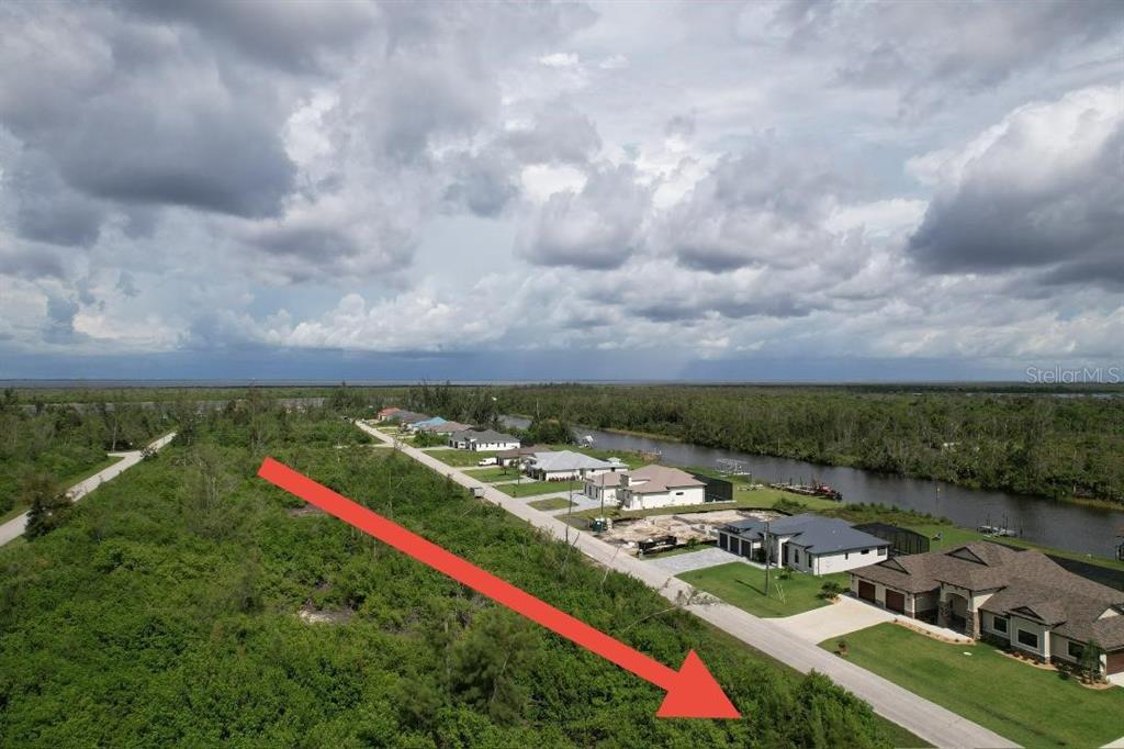An aerial view shows a vacant, tree-covered lot next to a paved road and houses — 16733 LIGGETT CIRCLE, PORT CHARLOTTE, FL
