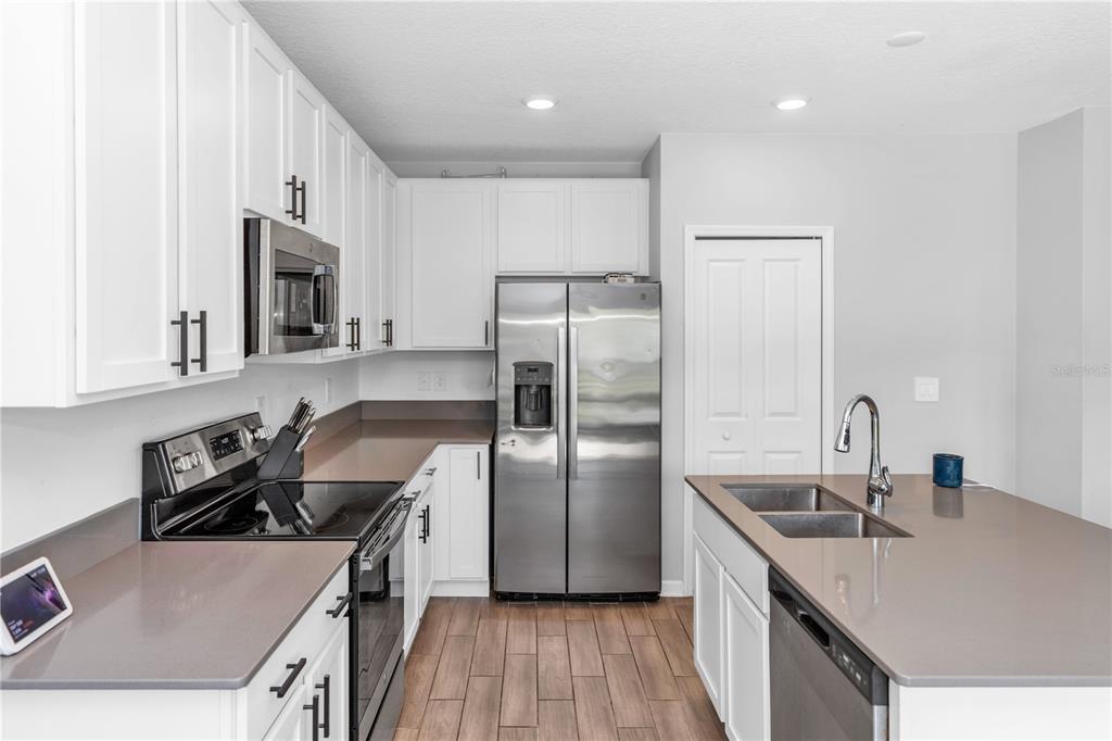 A modern kitchen features white cabinets, stainless steel appliances, and a large quartz-topped island — 1104 PEACH CREEK DRIVE, OSTEEN, FL