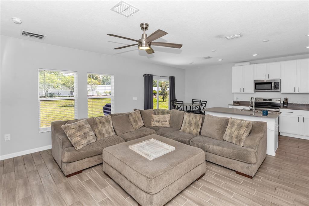 A living room with a large sectional sofa, ottoman, and an open kitchen in the background — 1104 PEACH CREEK DRIVE, OSTEEN, FL