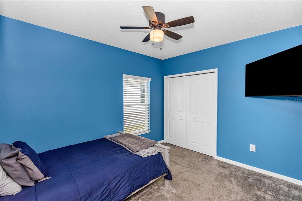 A bedroom features blue walls, a ceiling fan, a bed, and a closet with white doors — 1104 PEACH CREEK DRIVE, OSTEEN, FL