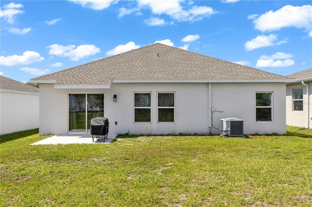 The exterior rear view of a single-story house with a patio, lawn, and AC unit — 1104 PEACH CREEK DRIVE, OSTEEN, FL