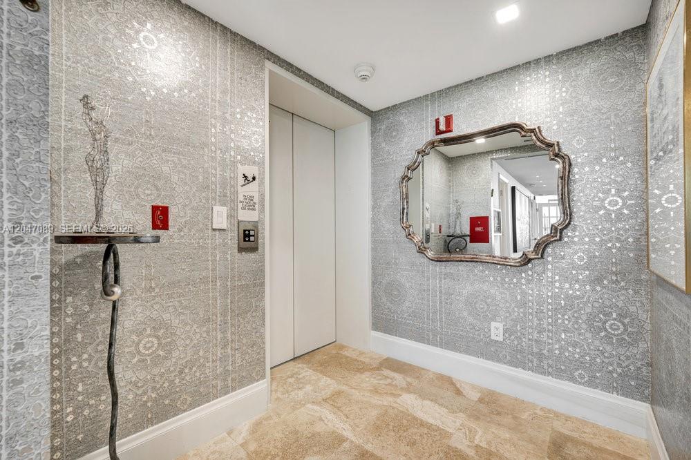 An elevator lobby features patterned gray wallpaper, a decorative mirror, and light-colored stone flooring — 1455 Ocean Dr # 904, Miami Beach FL 33139, MIAMI BEACH, FL