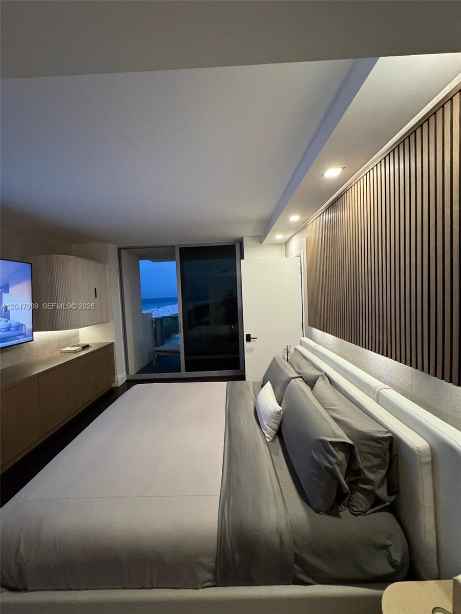 A modern bedroom features a bed with grey linens, wood slat wall paneling, and a balcony — 1455 Ocean Dr # 904, Miami Beach FL 33139, MIAMI BEACH, FL