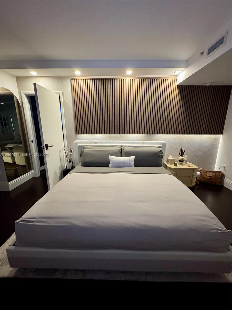 A bedroom features a bed centered against a wall with wood slat paneling and lighting — 1455 Ocean Dr # 904, Miami Beach FL 33139, MIAMI BEACH, FL