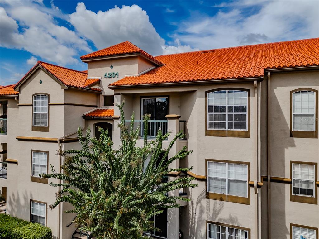 A multi-story apartment building exterior features tan stucco walls and a red tile roof — 4201 WOODSTORKS WALK WAY UNIT 3302, LUTZ, FL