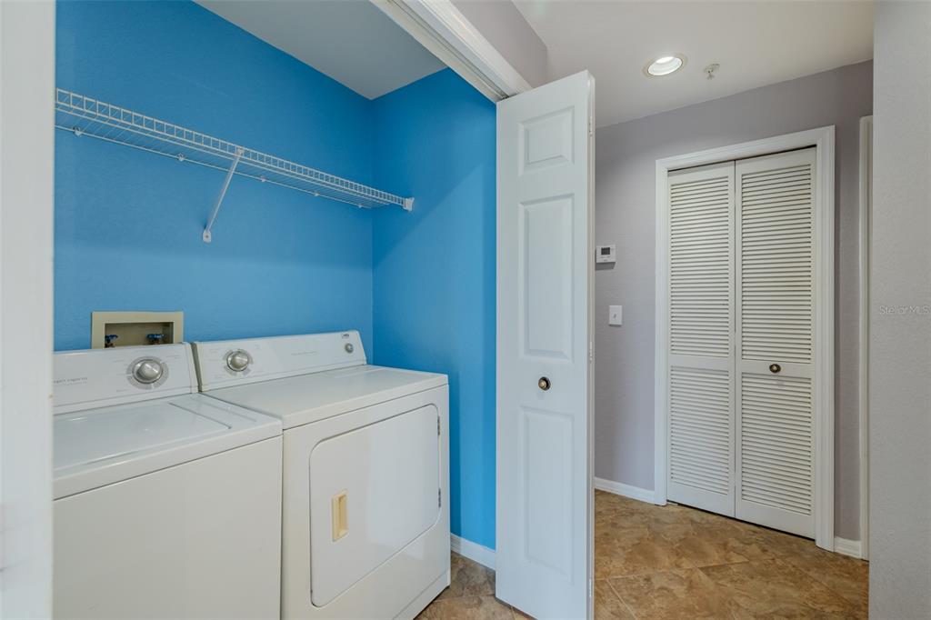 A laundry room features white appliances, blue walls, a wire shelf, and tile flooring — 4201 WOODSTORKS WALK WAY UNIT 3302, LUTZ, FL