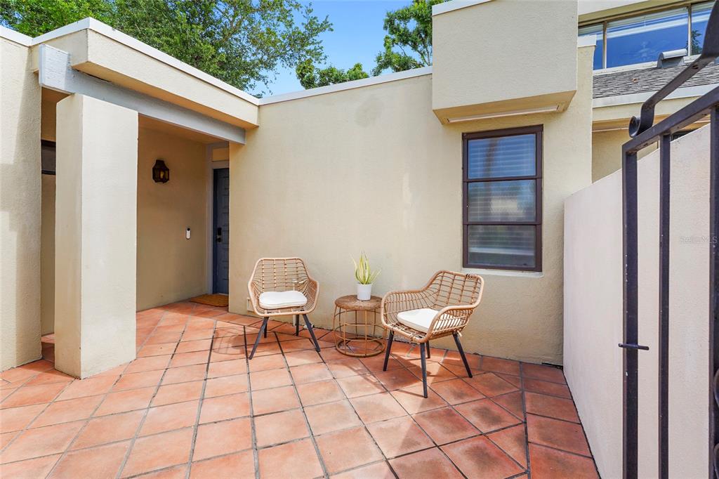 A patio features terracotta tile flooring, two wicker chairs, a small table, and an entryway — 2383 LAKESIDE MEWS UNIT D3, SARASOTA, FL