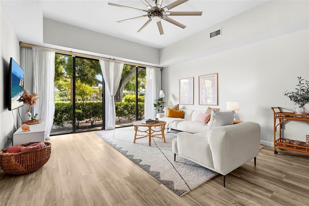 A bright living room features a white sofa, a patterned rug, and large sliding glass doors — 2383 LAKESIDE MEWS UNIT D3, SARASOTA, FL