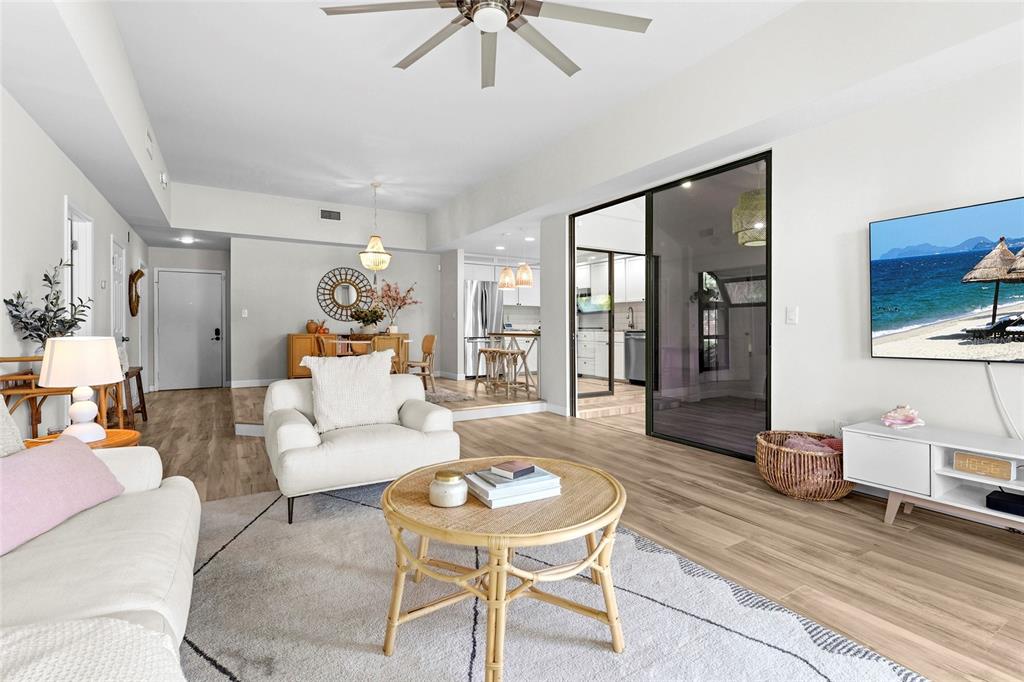 A living room features light wood flooring, a white sofa, and a glass-enclosed kitchen area — 2383 LAKESIDE MEWS UNIT D3, SARASOTA, FL