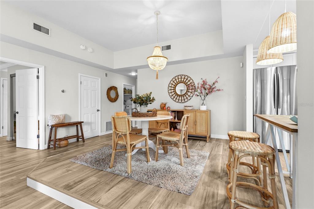 A dining area features a round table, rattan chairs, a chandelier, and a raised floor — 2383 LAKESIDE MEWS UNIT D3, SARASOTA, FL
