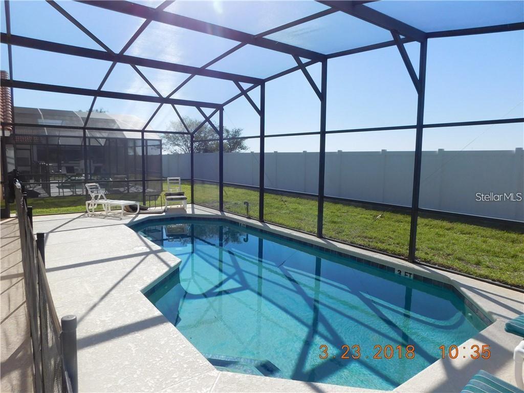 A swimming pool sits inside a screened-in lanai with a white fence in the background — 806 SOLANA CIRCLE, DAVENPORT, FL