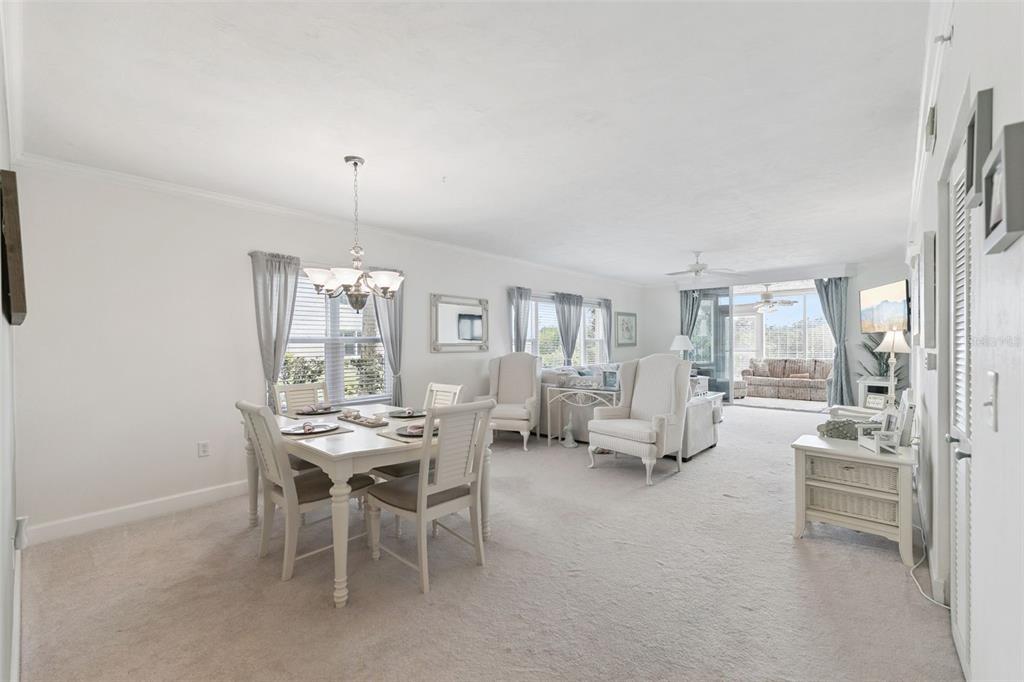 A bright living and dining area features white furniture, neutral carpeting, and a sunroom beyond — 426 BOUCHELLE DRIVE UNIT 101, NEW SMYRNA BEACH, FL