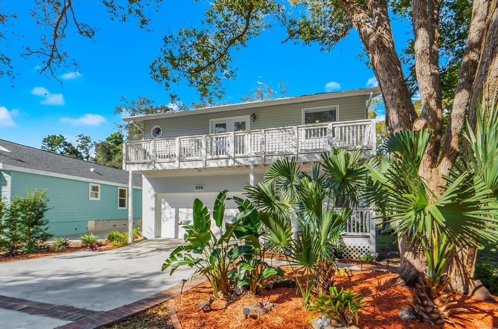 A two-story house with a white balcony, a concrete driveway, and tropical landscaping — 408 GEORGIA AVENUE, CRYSTAL BEACH, FL