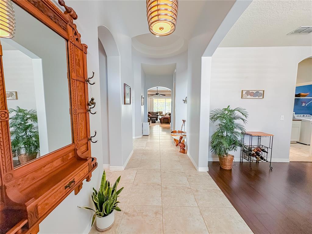 A hallway with tile flooring connects a foyer with a wooden mirror to a living area — 1528 BLUE GRASS BOULEVARD, DELAND, FL