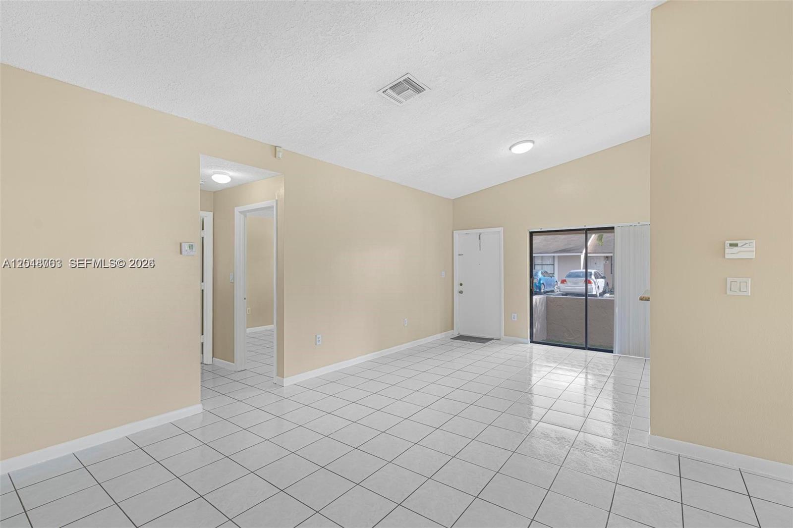 An empty living room features white tile flooring, beige walls, and a sliding glass door — 7730 SW 156th Ct # A145, Miami FL 33193, MIAMI, FL