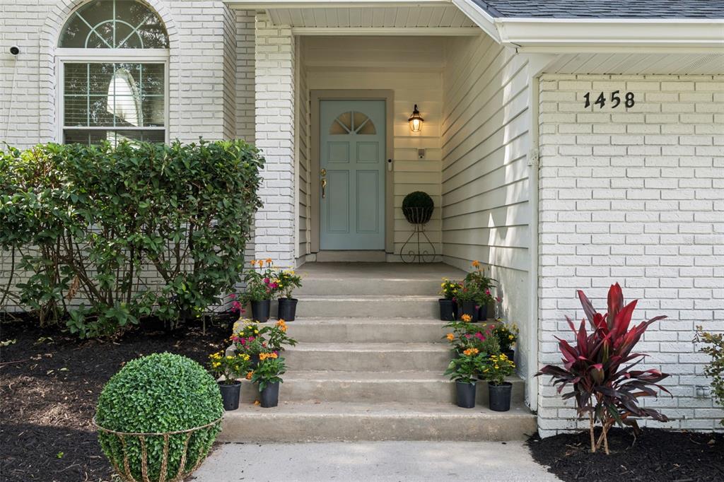 A light blue front door is centered at the top of concrete steps with potted flowers — 1458 ROYAL CIRCLE, APOPKA, FL