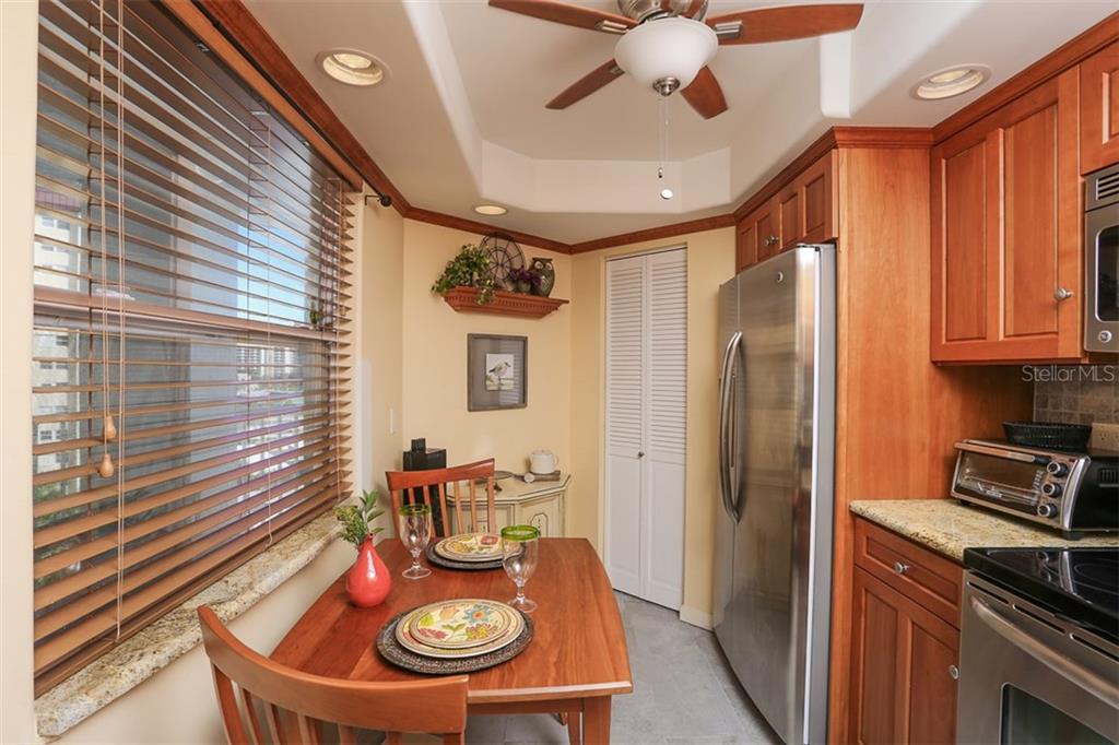 A kitchen features wooden cabinets, stainless steel appliances, a dining table, and a window with blinds — 1770 BENJAMIN FRANKLIN DRIVE UNIT 603, SARASOTA, FL