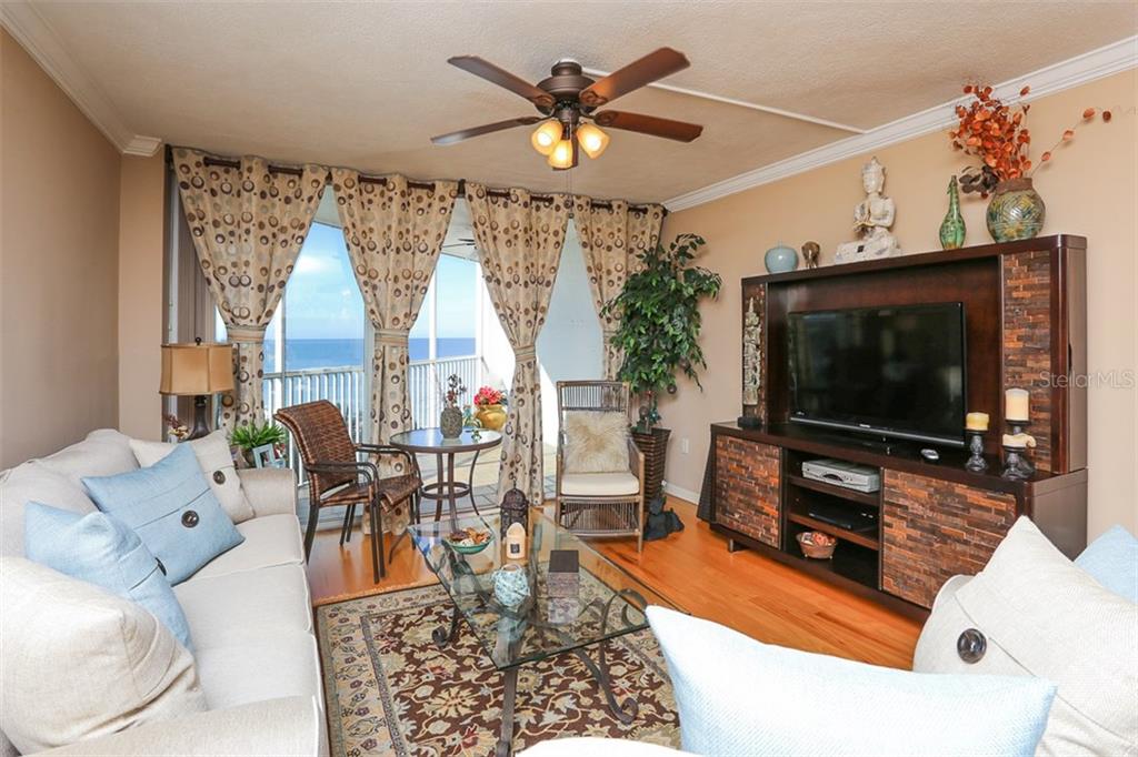 A living room features hardwood floors, a ceiling fan, and a balcony with ocean views — 1770 BENJAMIN FRANKLIN DRIVE UNIT 603, SARASOTA, FL