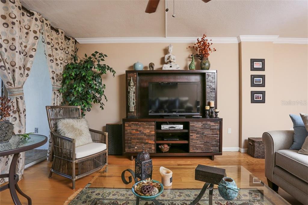 A living room features a wooden entertainment center, a rattan chair, and a glass coffee table — 1770 BENJAMIN FRANKLIN DRIVE UNIT 603, SARASOTA, FL