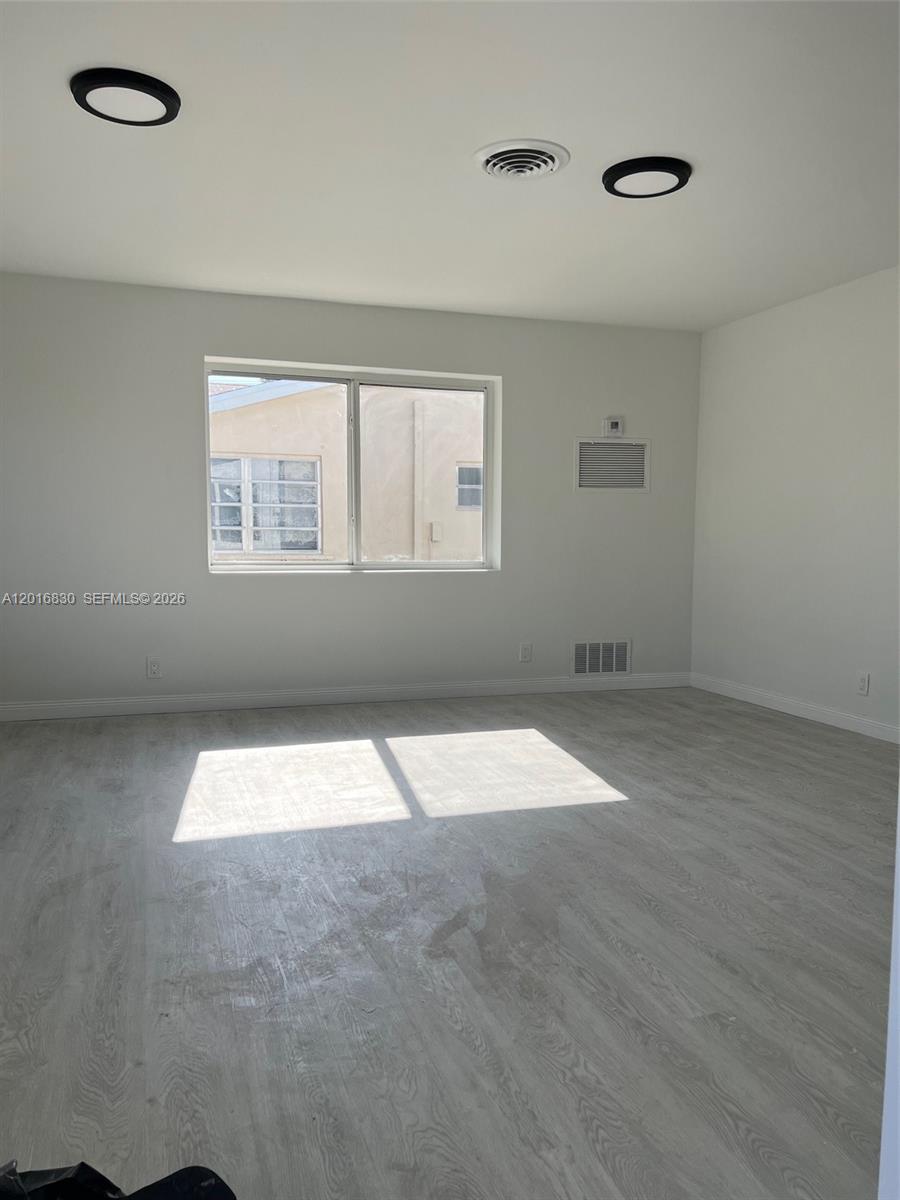 An empty room features light wood-look flooring, white walls, recessed lighting, and a window — FORT LAUDERDALE, FL