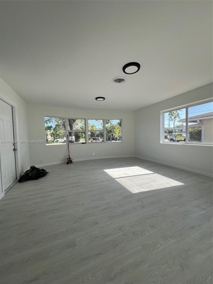 An empty room features light-colored wood-look flooring, white walls, and large windows — FORT LAUDERDALE, FL