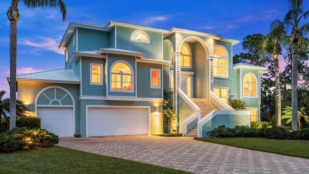 A three-story teal house with a multi-car garage and an elevated front staircase at dusk — 2806 BAY VISTA COURT, NEW SMYRNA BEACH, FL