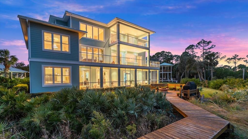A three-story teal house with a wooden walkway leading to a screened-in ground floor patio — 2806 BAY VISTA COURT, NEW SMYRNA BEACH, FL